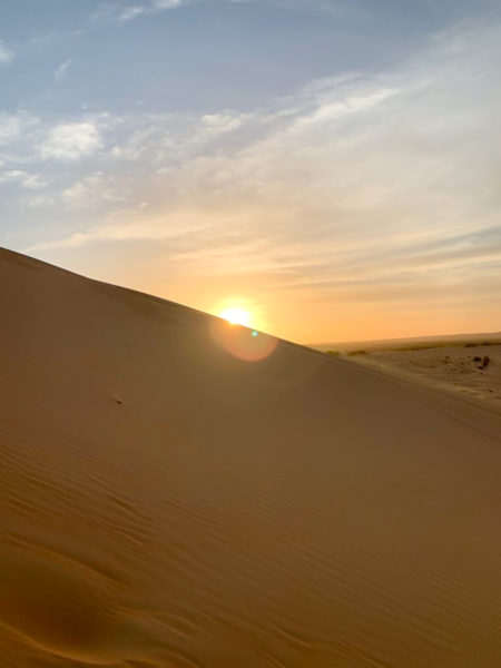The sun sets behind the sloped edge of a huge dune in Azouega