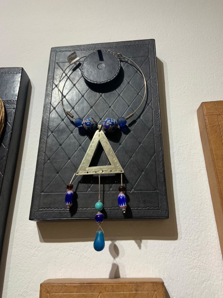 A Mauritanian-made necklace with a triangle pendent and danlging beads hangs on a wall hook