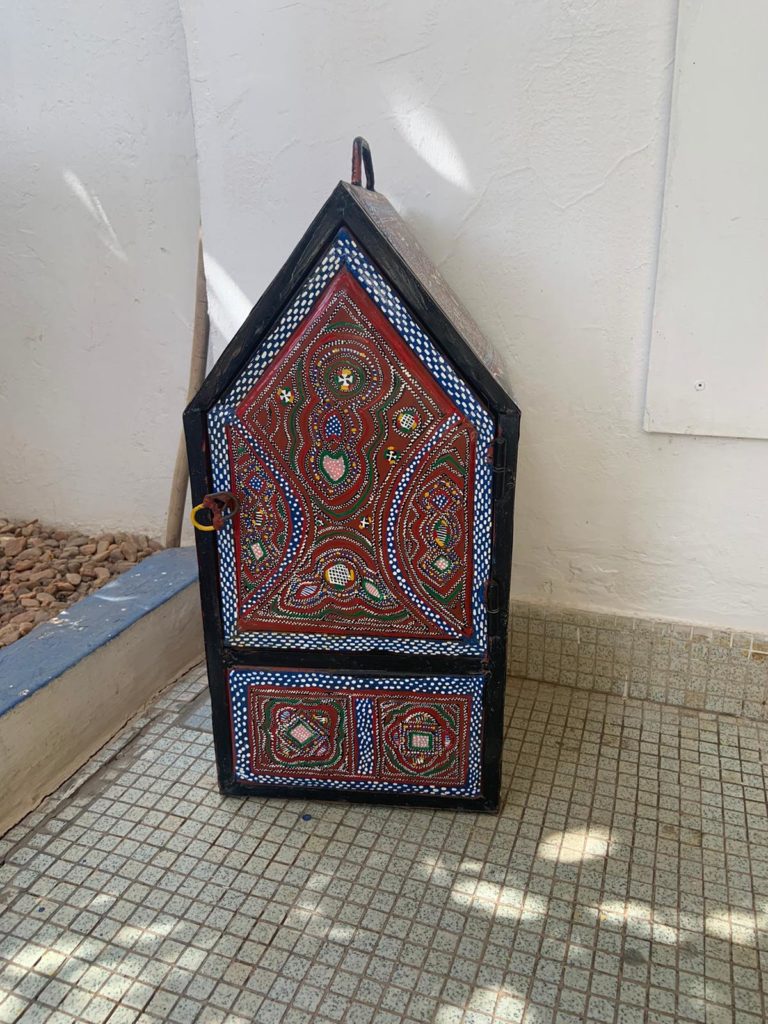 A small cabinet with intricately beaded door sits on a tile floor