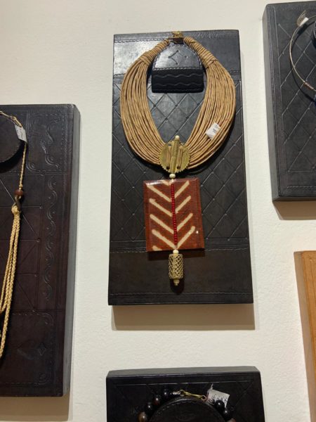 A Mauritanian-made necklace with a large patterned pendant hangs on a wall hook